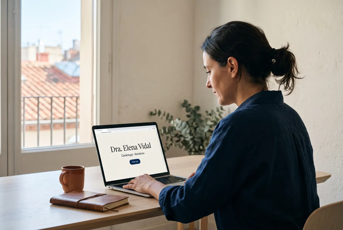 Una médica revisa la web de su consulta en un portátil, con la página de inicio en pantalla.